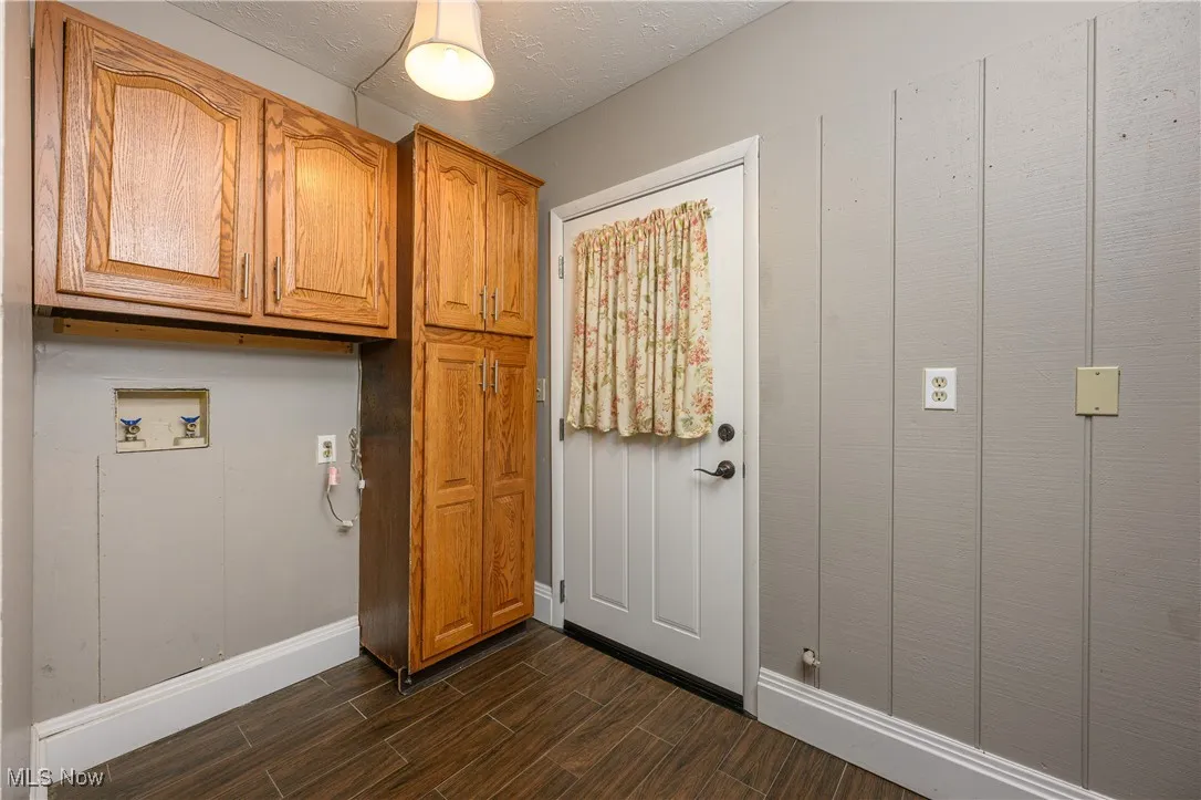Washroom with a textured ceiling, wood tiled floors, cabinet space, and washer hookup