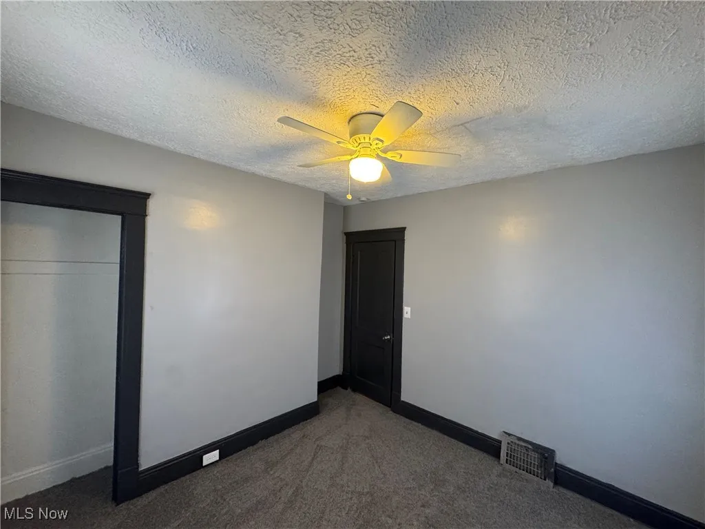 Unfurnished bedroom with a textured ceiling, carpet floors, and a ceiling fan