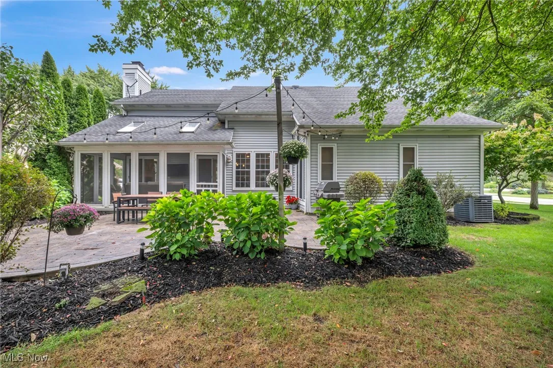 Back of property featuring a sunroom, roof with shingles, a chimney, and a patio area