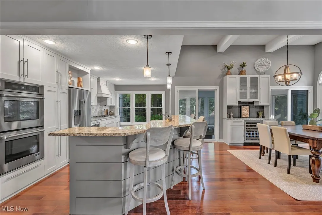 Kitchen featuring tasteful backsplash, appliances with stainless steel finishes, light stone countertops, white cabinetry, and beamed ceiling