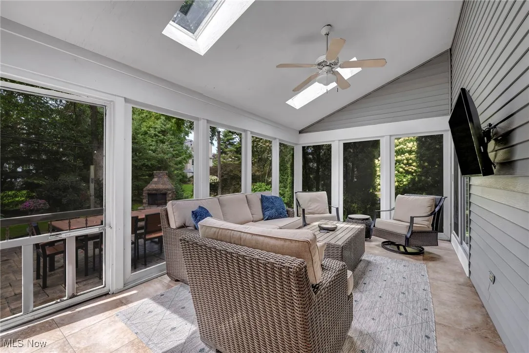 Sunroom featuring a skylight, vaulted ceiling, a ceiling fan, an outdoor living space with a fireplace, and a patio area