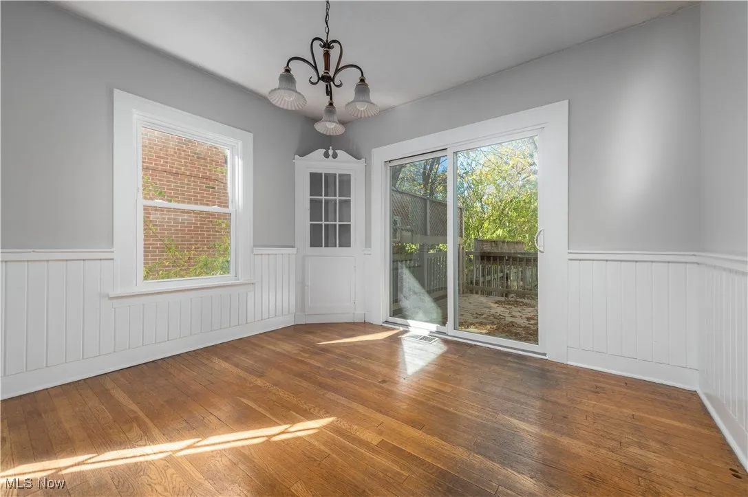 Unfurnished dining area featuring wood-type flooring, wainscoting, and a chandelier