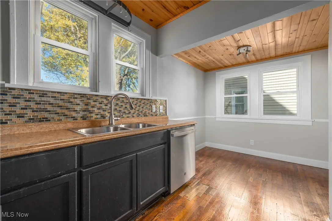 Kitchen with wood ceiling, tasteful backsplash, dark wood finished floors, stainless steel dishwasher, and dark cabinets