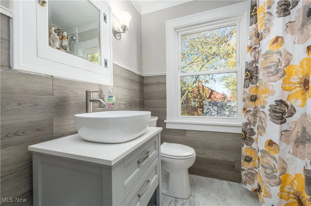Full bathroom with tile walls, vanity, a shower with shower curtain, ornamental molding, and a wainscoted wall