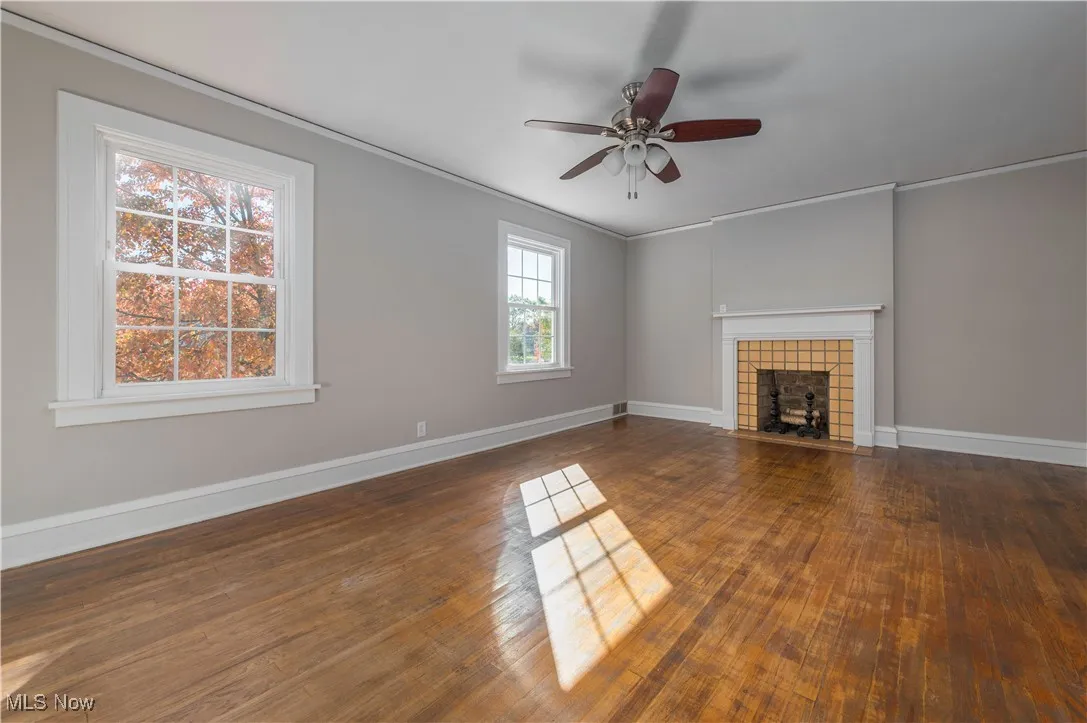 Unfurnished living room featuring ornamental molding, a tile fireplace, dark wood-type flooring, and a ceiling fan