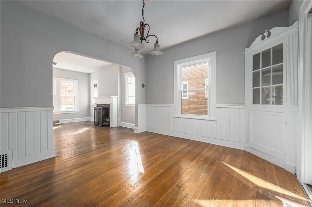 Unfurnished dining area with arched walkways, wood-type flooring, a fireplace with flush hearth, and a wainscoted wall