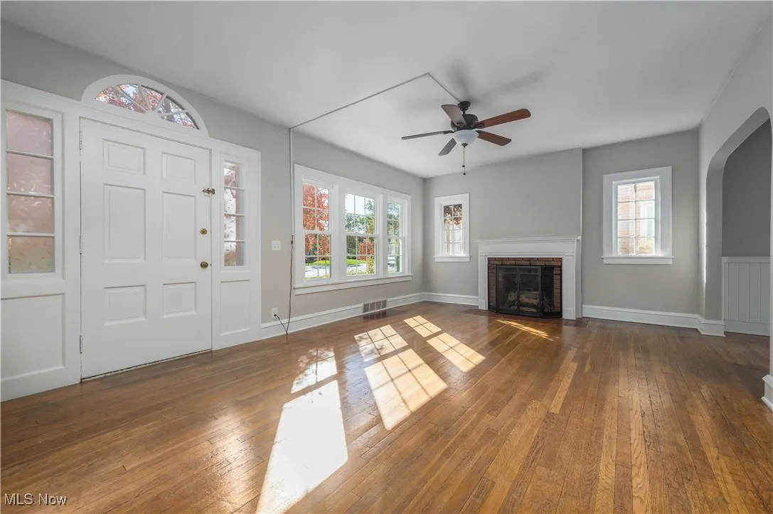 Unfurnished living room with arched walkways, dark wood-style floors, a fireplace, and a ceiling fan