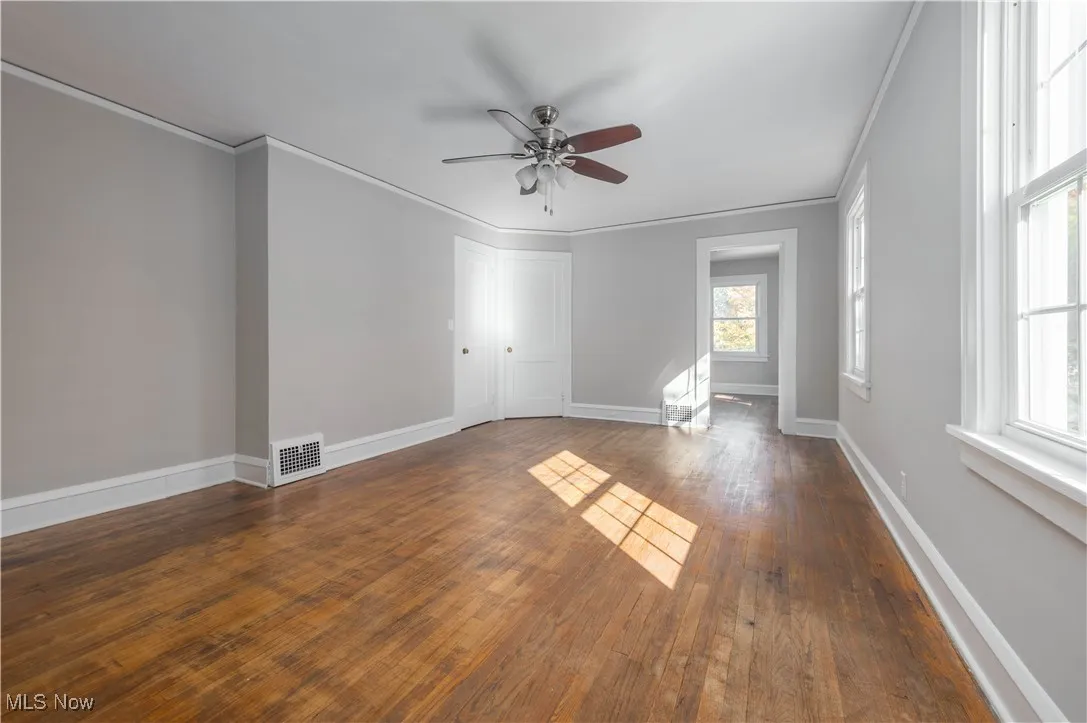 Empty room with dark wood-type flooring, ornamental molding, and a ceiling fan