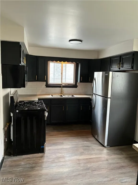 Kitchen with dark cabinetry, black appliances, light wood-style floors, and backsplash