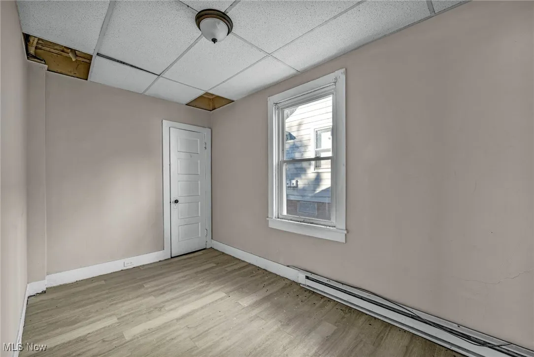 Empty room with light wood-style floors, a paneled ceiling, and baseboard heating