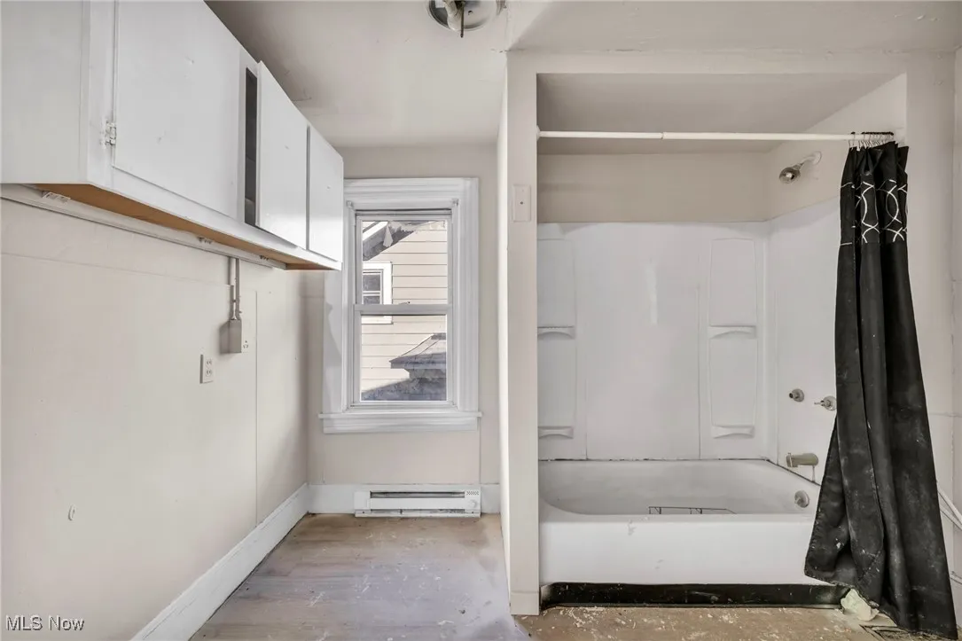 Full bath featuring shower / tub combo with curtain, a baseboard radiator, and wood finished floors