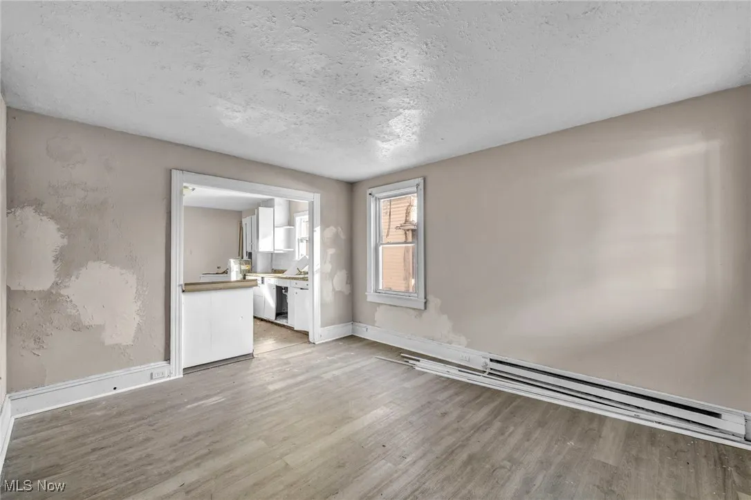 Unfurnished living room with a textured ceiling, light wood-type flooring, and a baseboard radiator