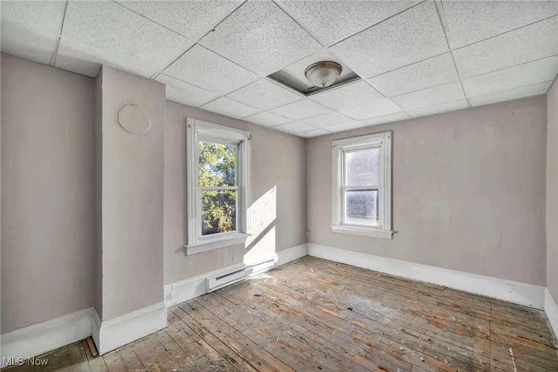Unfurnished room featuring wood-type flooring, a baseboard heating unit, and a paneled ceiling