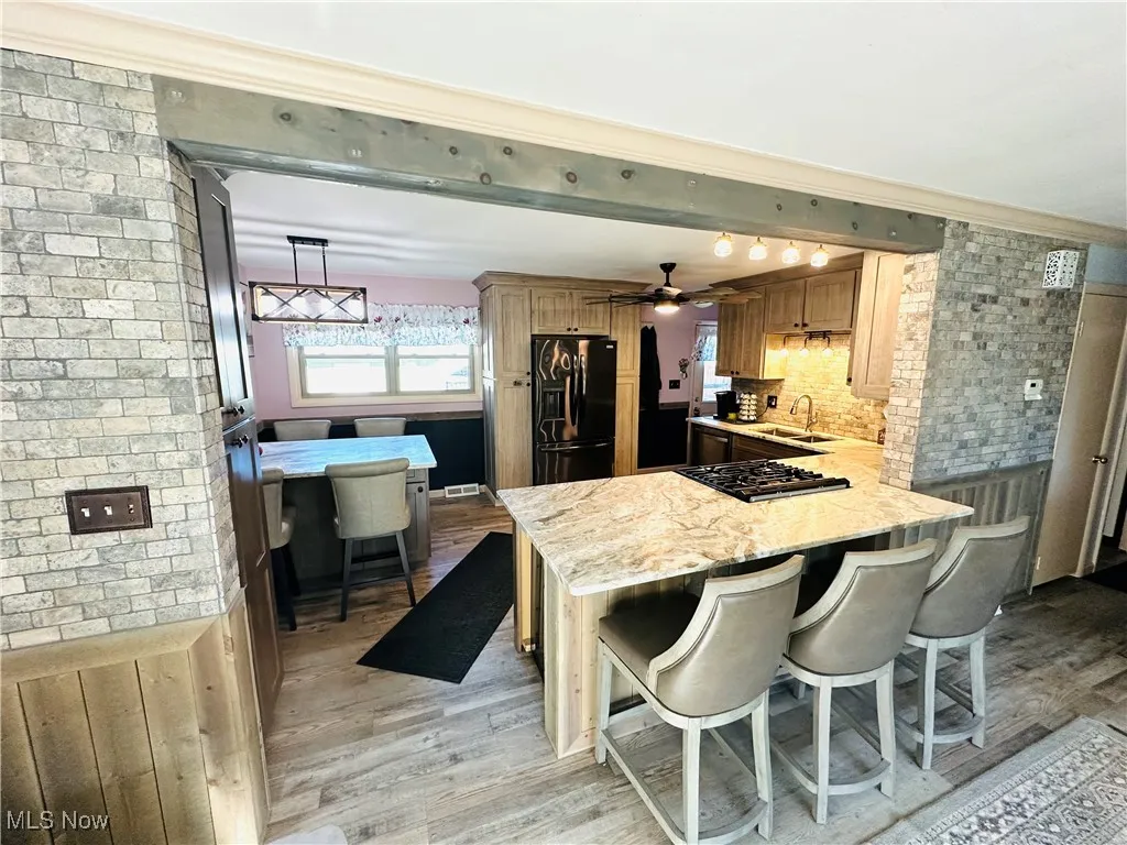 Kitchen featuring a kitchen bar, light wood-style floors, ceiling fan, a peninsula, and black fridge with ice dispenser