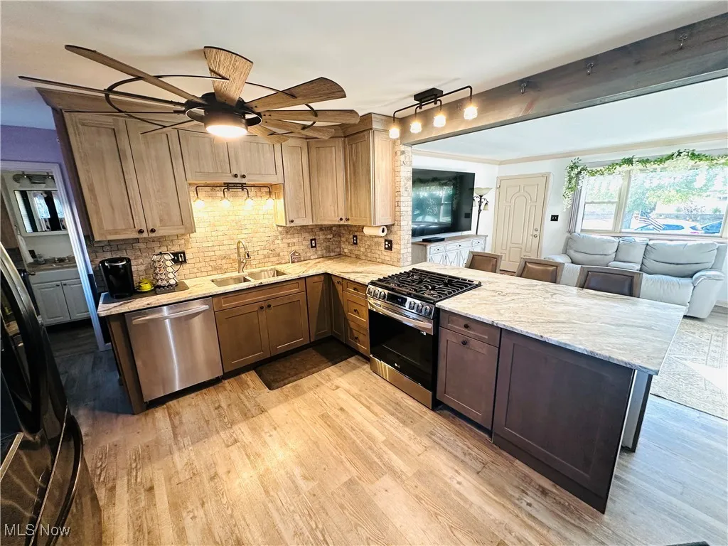 Kitchen featuring appliances with stainless steel finishes, a peninsula, light stone countertops, backsplash, and ornamental molding