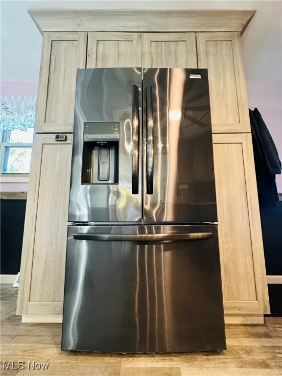 Kitchen view of light brown cabinets, light wood finished floors, and stainless steel fridge