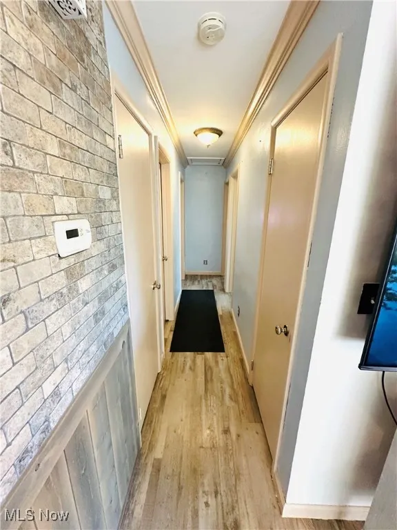 Hallway with light wood-style floors and crown molding