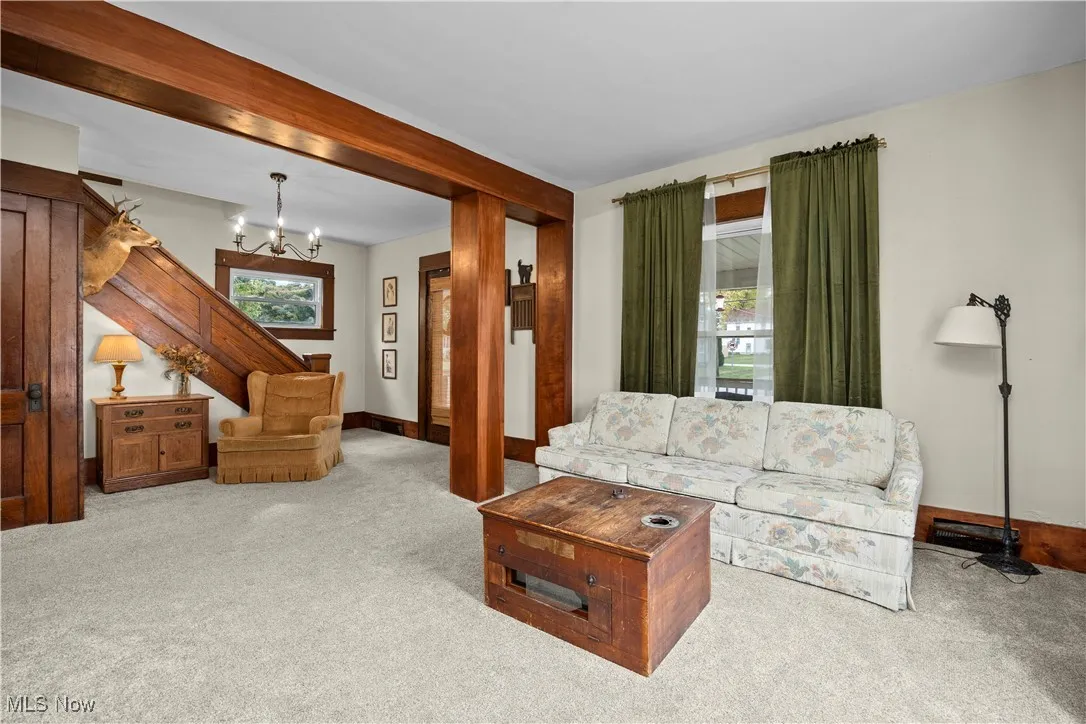 Living room featuring carpet, beam ceiling, and a chandelier