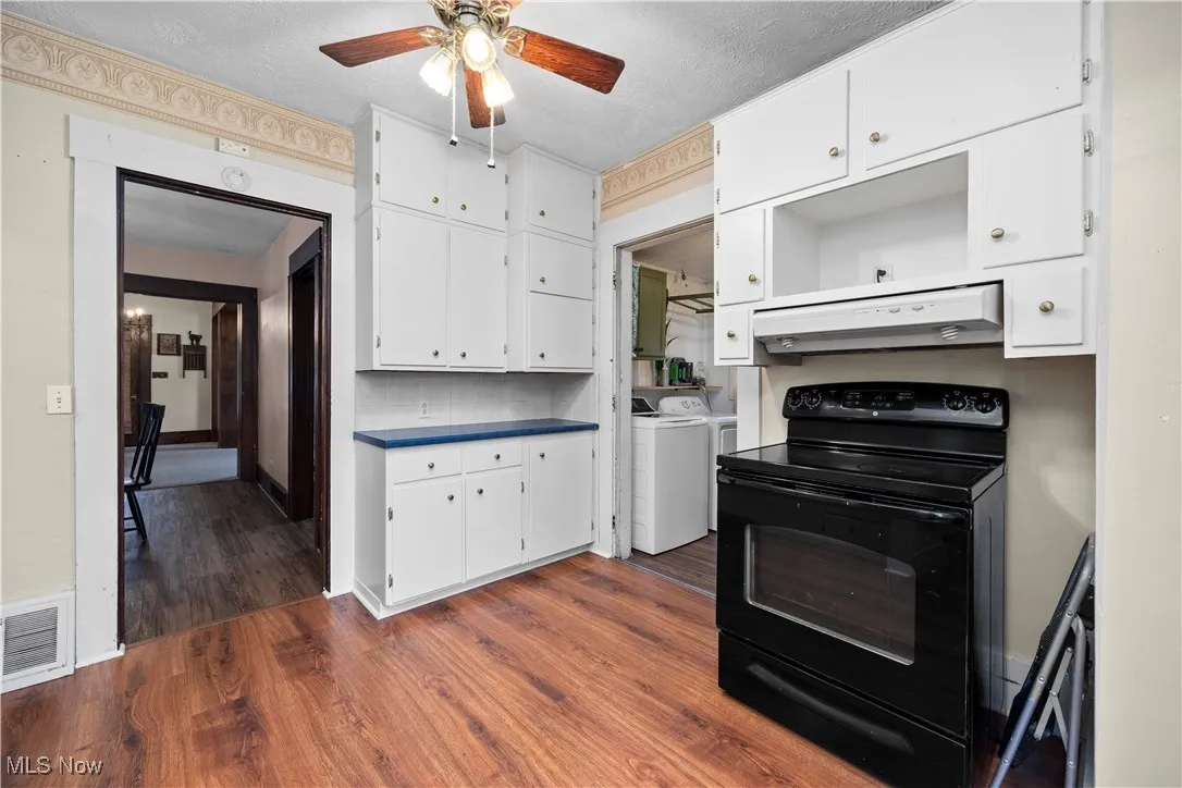 Kitchen featuring black range with electric stovetop, dark wood-style floors, white cabinets, extractor fan, and dark countertops