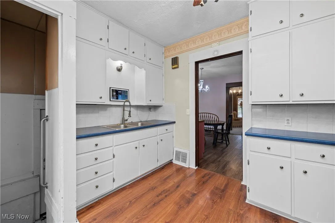 Kitchen with dark wood-style floors, backsplash, dark countertops, white cabinets, and a textured ceiling