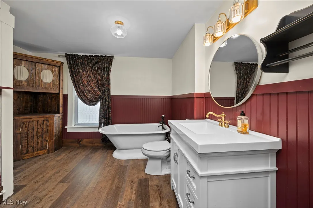 Full bathroom with vanity, a soaking tub, dark wood-style flooring, and a wainscoted wall