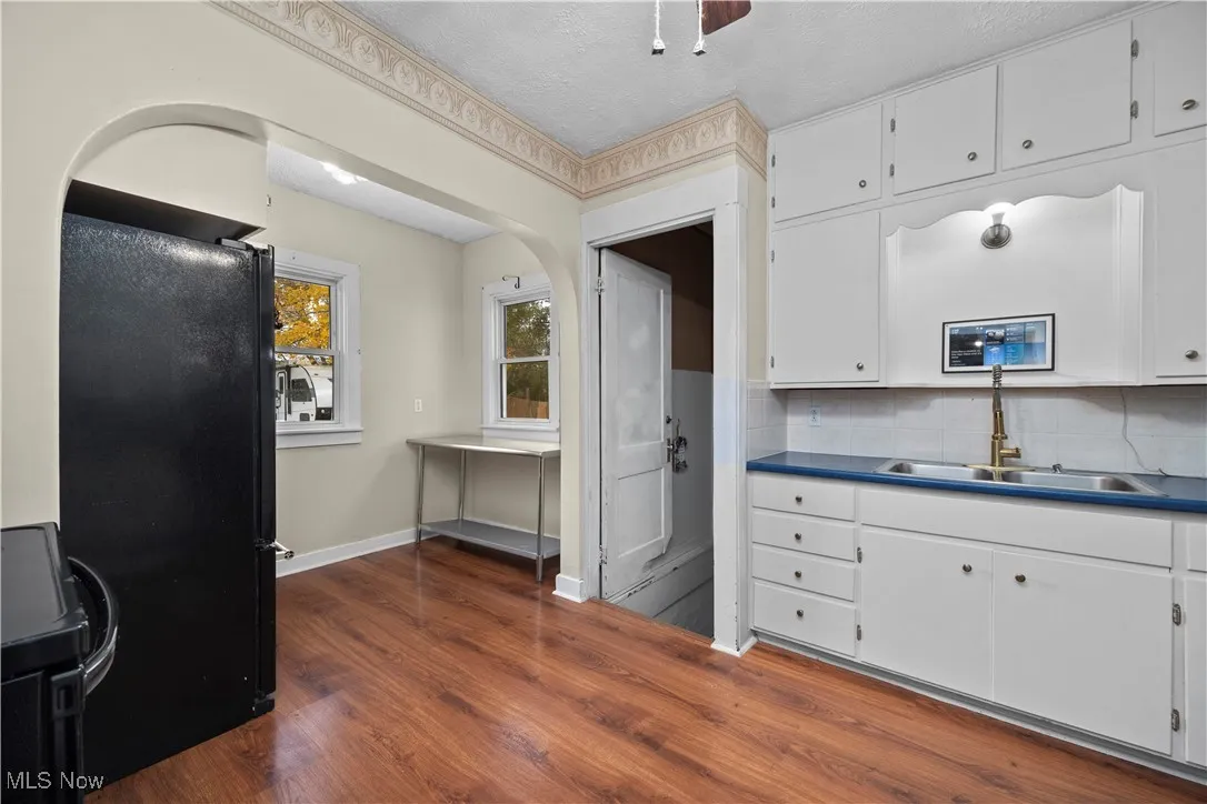 Kitchen with black appliances, white cabinets, backsplash, dark wood-type flooring, and a ceiling fan