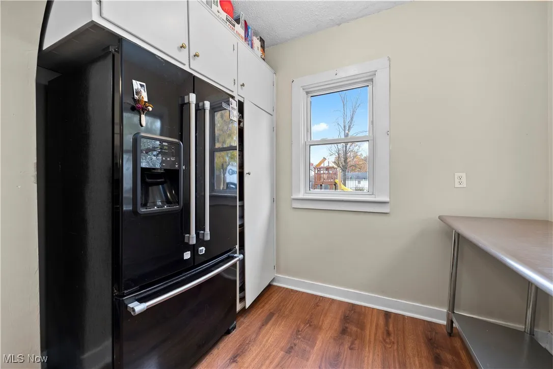 Kitchen featuring black fridge, dark wood-style flooring, a textured ceiling, and white cabinets