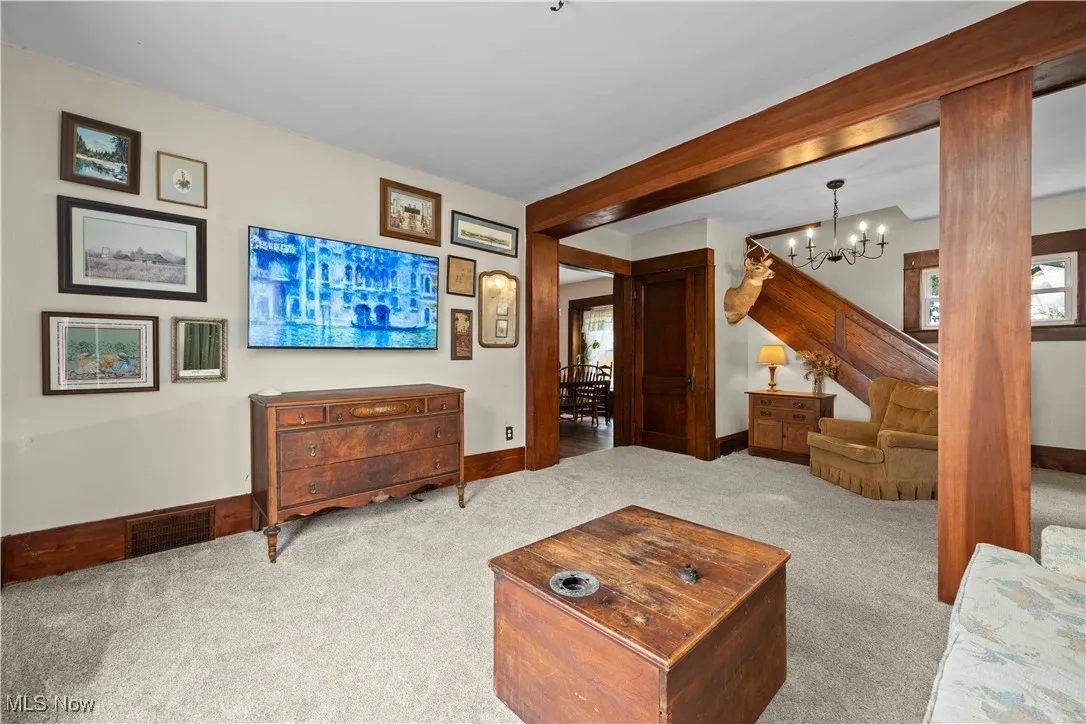 Living area featuring carpet, beamed ceiling, and a chandelier