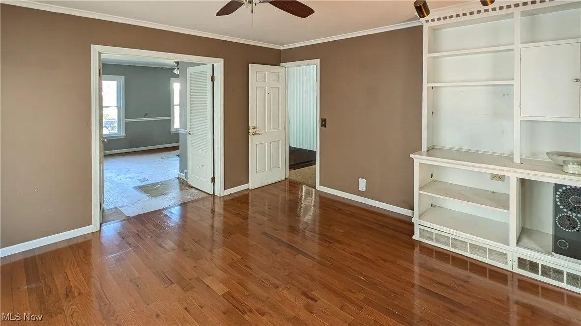 Unfurnished bedroom with ornamental molding, dark wood-style flooring, and a ceiling fan