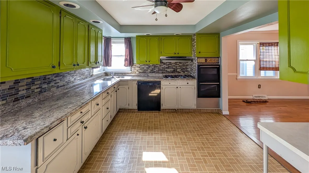 Kitchen with tasteful backsplash, brick patterned floors, black appliances, and a raised ceiling