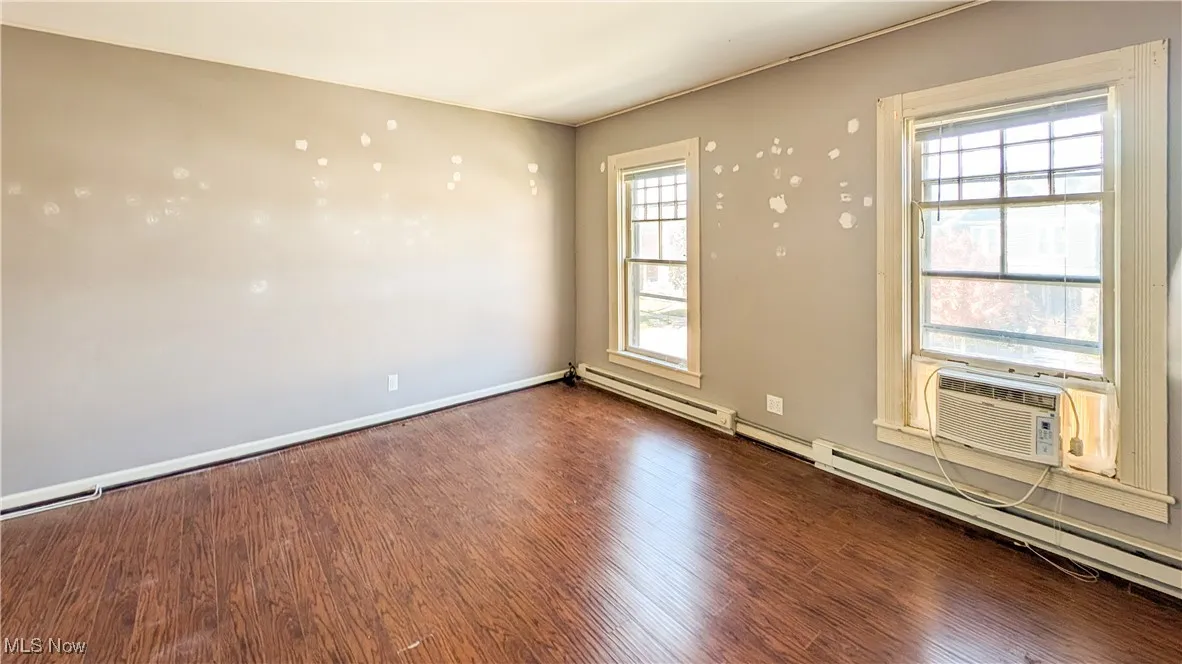 Unfurnished room featuring wood finished floors, baseboard heating, and cooling unit