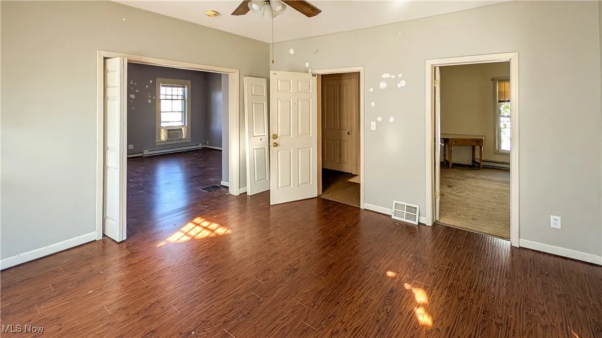 Unfurnished bedroom with dark wood-style flooring, ceiling fan, and baseboard heating
