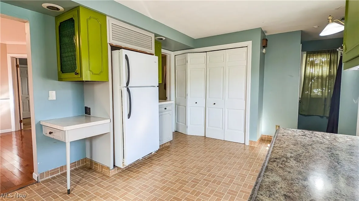 Kitchen featuring green cabinetry, freestanding refrigerator, brick patterned floors, and light countertops