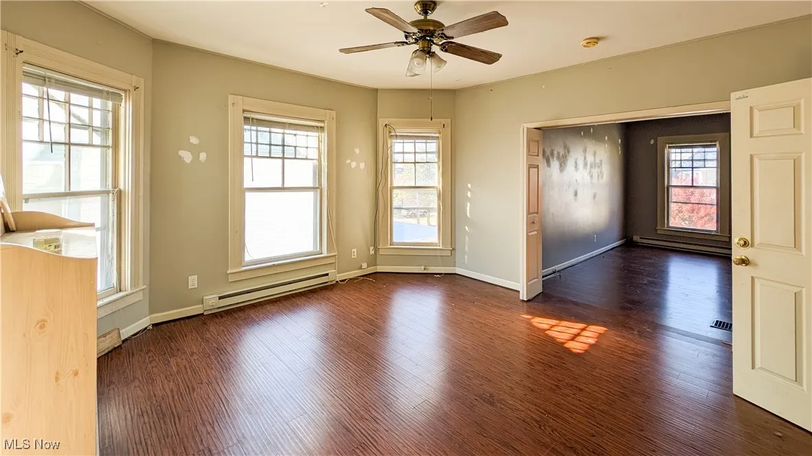 Unfurnished room featuring baseboard heating, dark wood finished floors, and ceiling fan