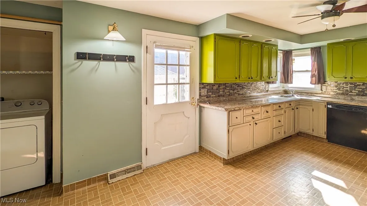 Kitchen featuring brick patterned flooring, washer / clothes dryer, black dishwasher, and tasteful backsplash