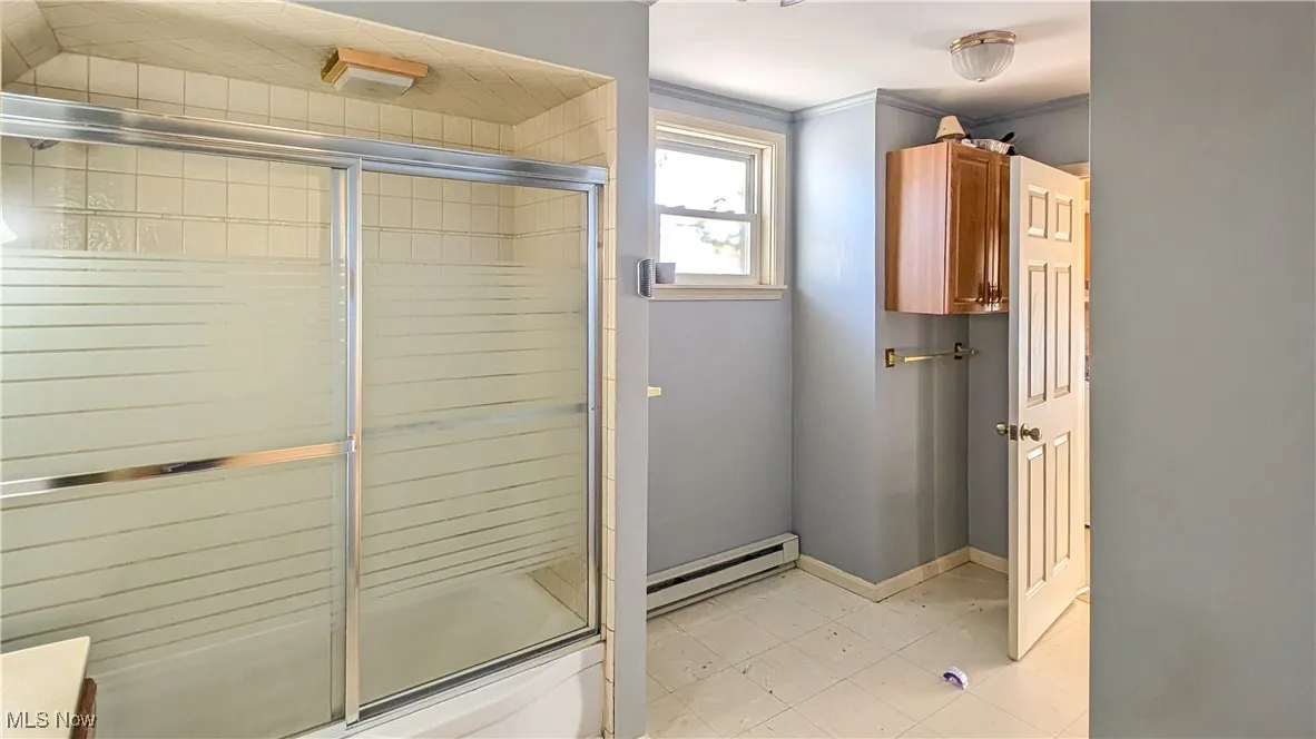 Full bathroom featuring a baseboard heating unit, a shower stall, and ornamental molding