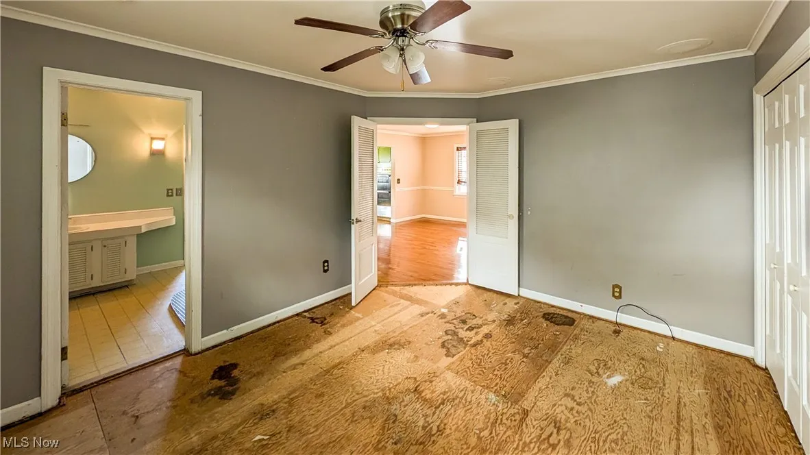 Unfurnished bedroom featuring ornamental molding, ensuite bathroom, ceiling fan, and a closet