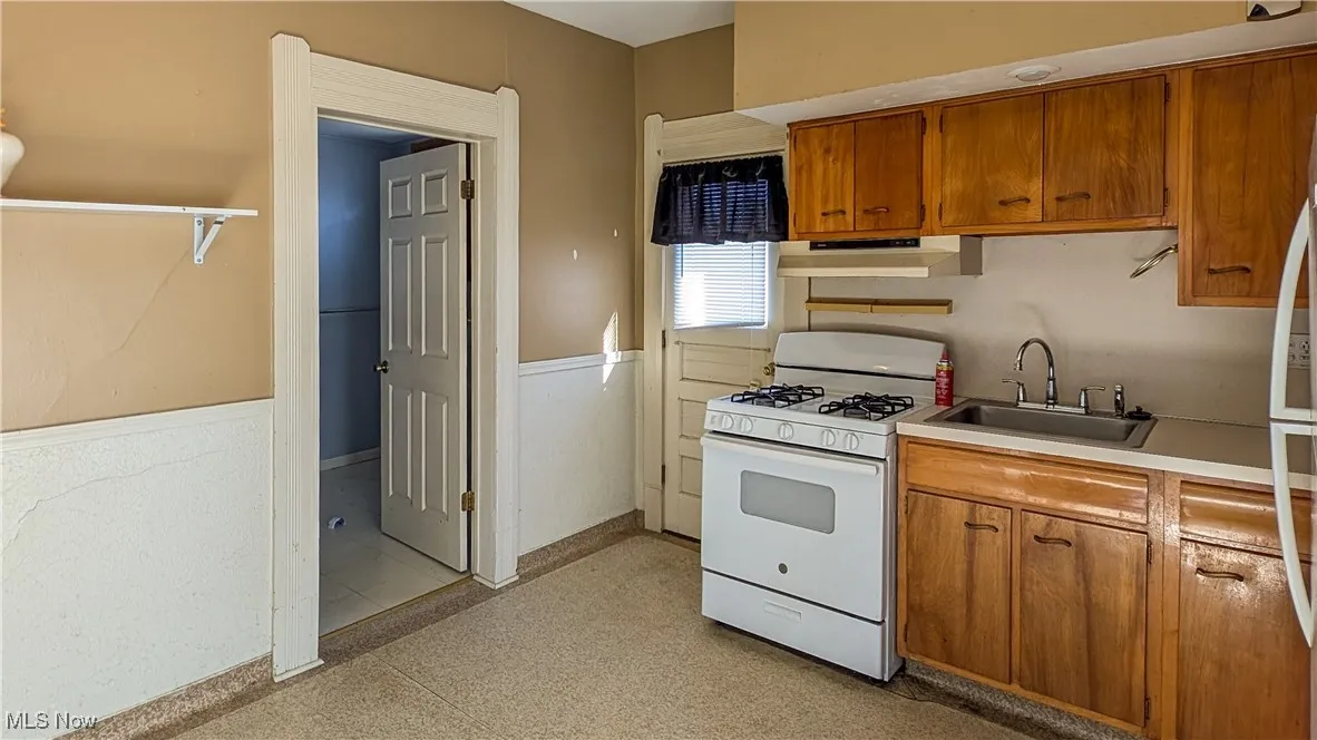 Kitchen featuring white appliances, brown cabinets, light countertops, under cabinet range hood, and light flooring