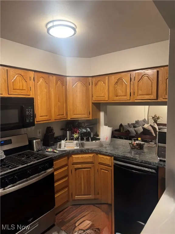 Kitchen featuring black appliances, brown cabinetry, dark countertops, and wood finished floors