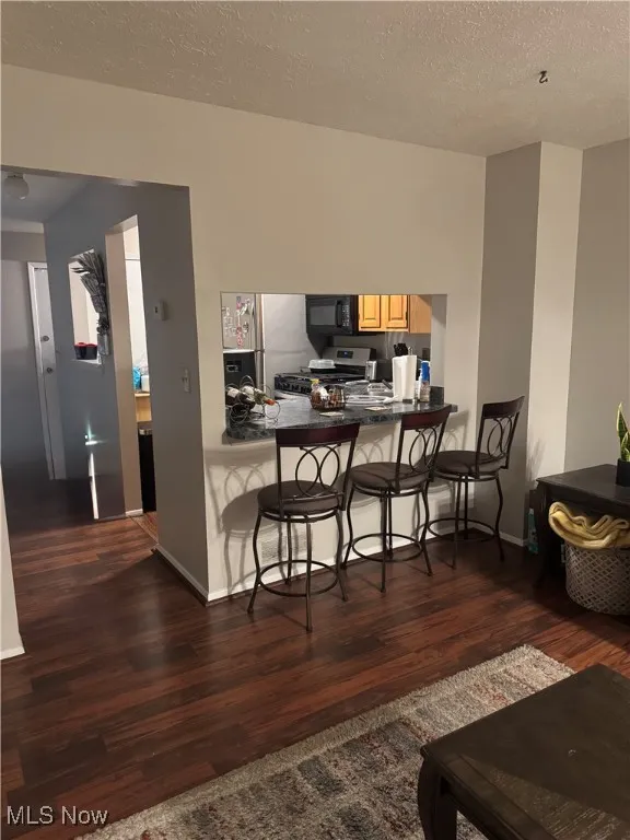 Kitchen featuring dark countertops, dark wood-style flooring, a breakfast bar, a peninsula, and a textured ceiling