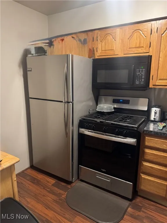 Kitchen with stainless steel appliances, dark wood-style flooring, and brown cabinets