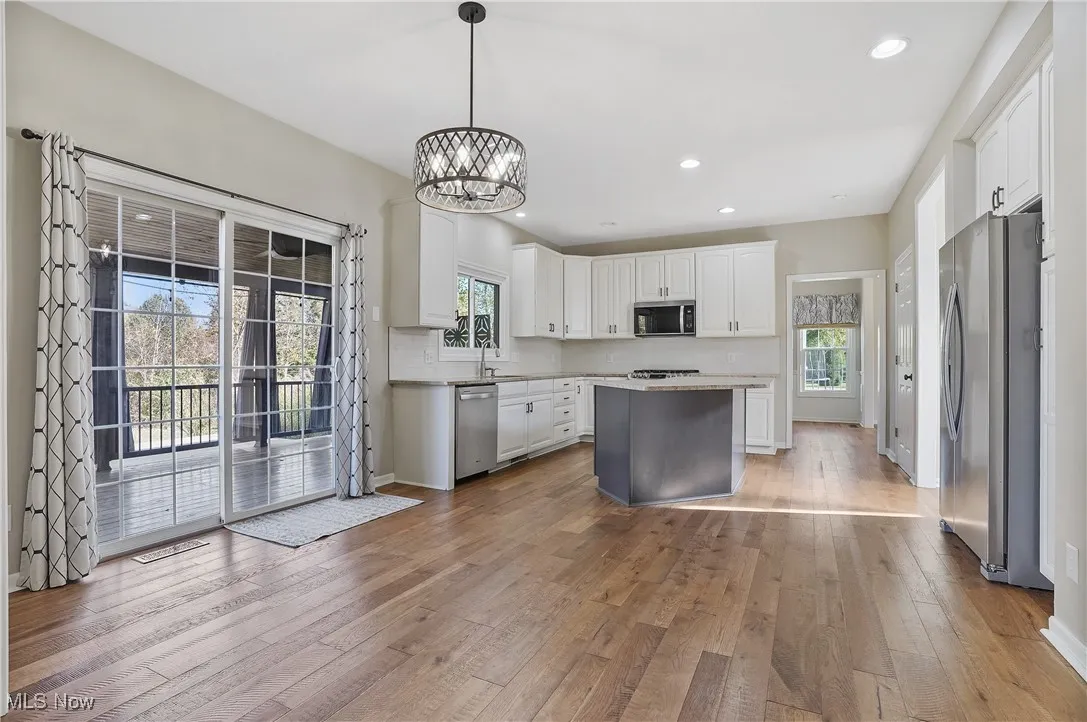 Kitchen with stainless steel appliances, pendant lighting, a chandelier, white cabinetry, and light wood finished floors