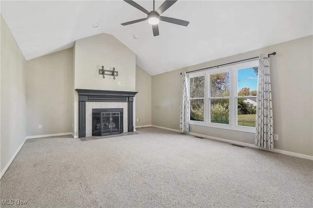 Unfurnished living room with carpet, a fireplace, high vaulted ceiling, and ceiling fan