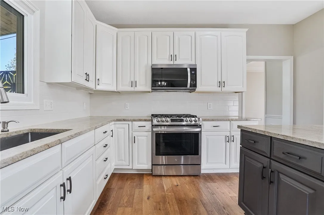 Kitchen featuring appliances with stainless steel finishes, white cabinets, light wood-style flooring, light stone counters, and backsplash