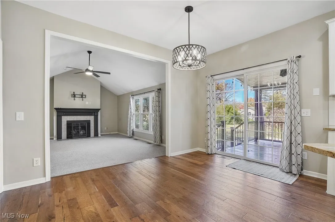 Unfurnished living room featuring dark wood-type flooring, lofted ceiling, a ceiling fan, a tile fireplace, and a chandelier
