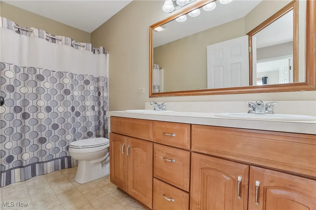 Bathroom featuring double vanity, a shower with shower curtain, and light floors