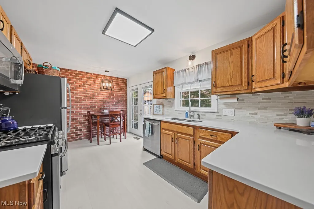 Kitchen featuring appliances with stainless steel finishes, brown cabinetry, light countertops, and brick wall