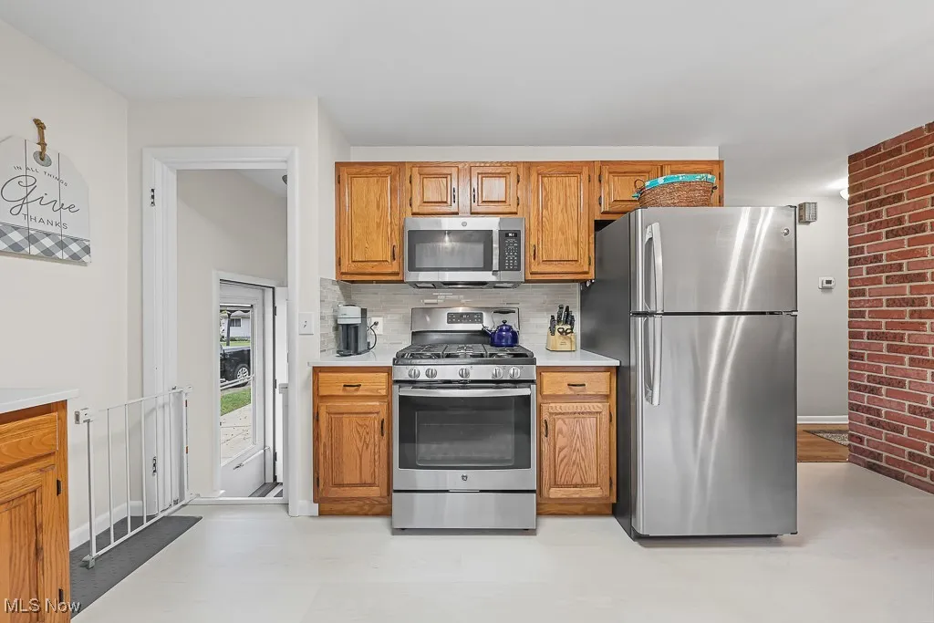 Kitchen featuring appliances with stainless steel finishes, light countertops, decorative backsplash, brown cabinetry, and brick wall