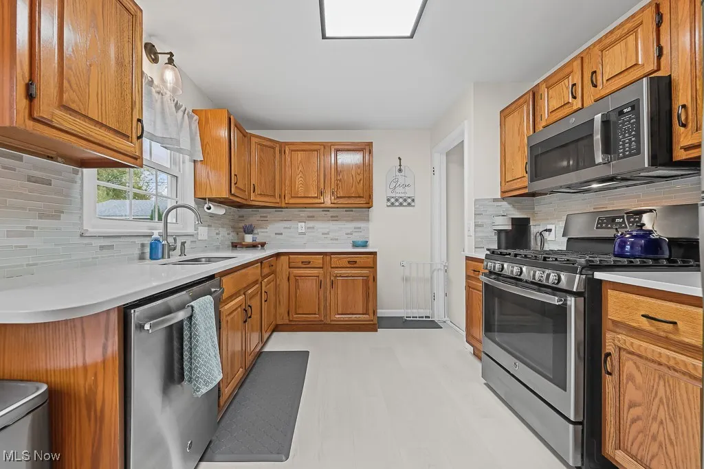 Kitchen featuring backsplash, appliances with stainless steel finishes, brown cabinetry, light countertops, and lofted ceiling