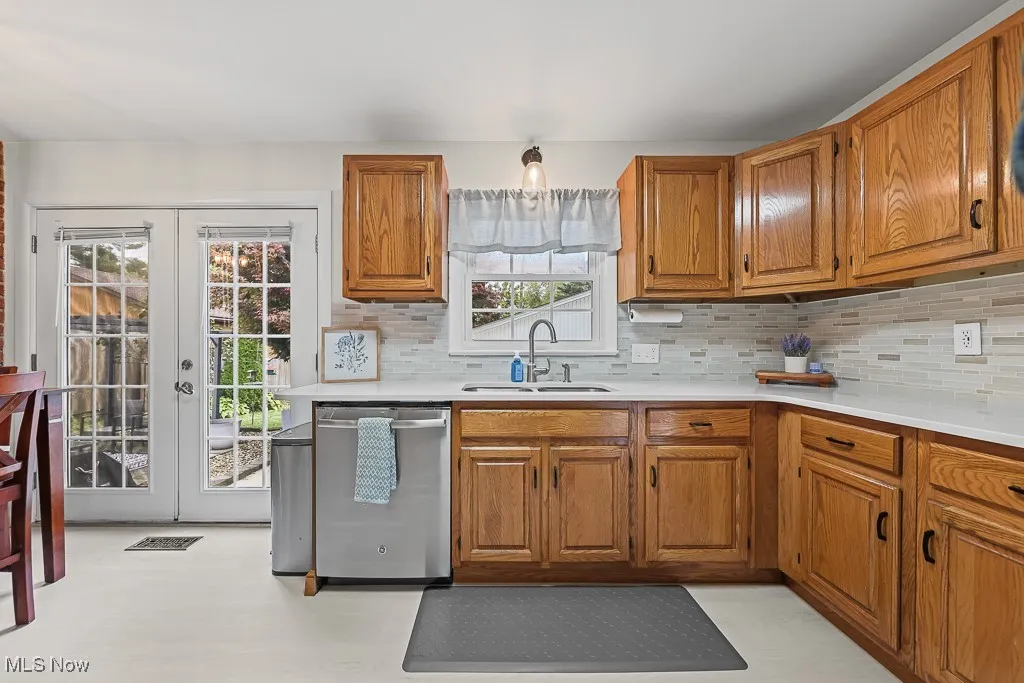 Kitchen featuring brown cabinetry, stainless steel dishwasher, tasteful backsplash, and french doors